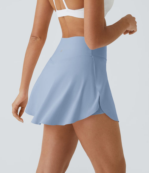 "Femme portant une jupe-short de sport bleu clair, soulevant légèrement la jupe pour montrer le short intégré en dessous."